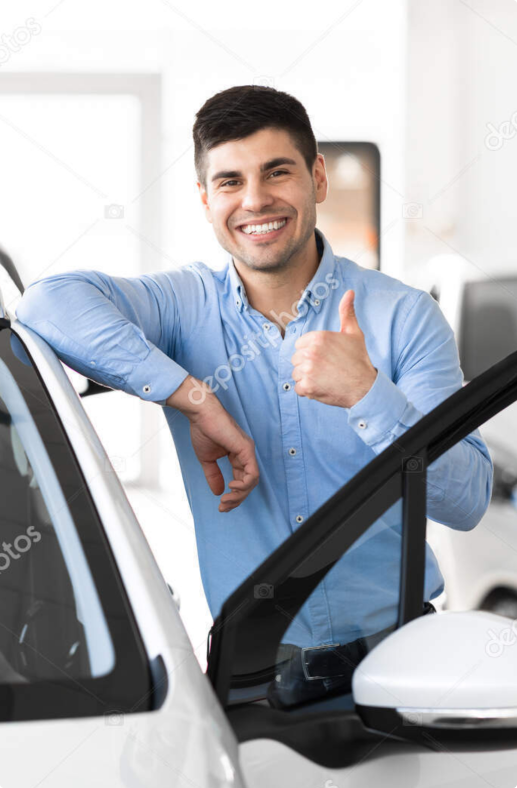 Smiling car salesman giving thumbs up in a car showroom, promoting lease options — stock photo.