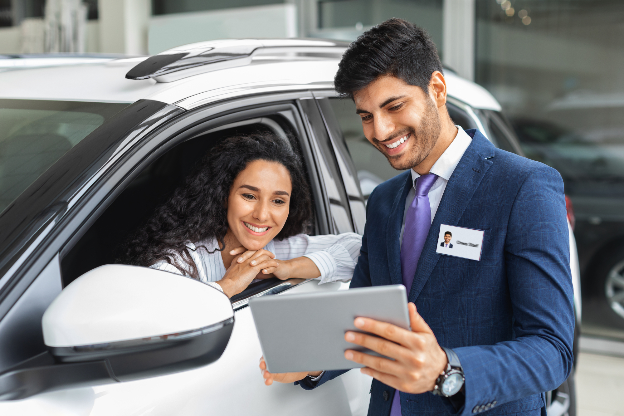 A man and woman exploring a novated lease option by diligently researching various lease terms and conditions on a tablet inside a car showroom.