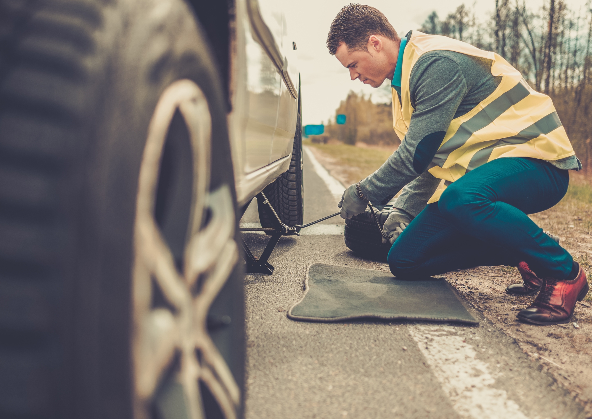 A man fixing a tire on the side of the road while considering a novated lease for his vehicle.