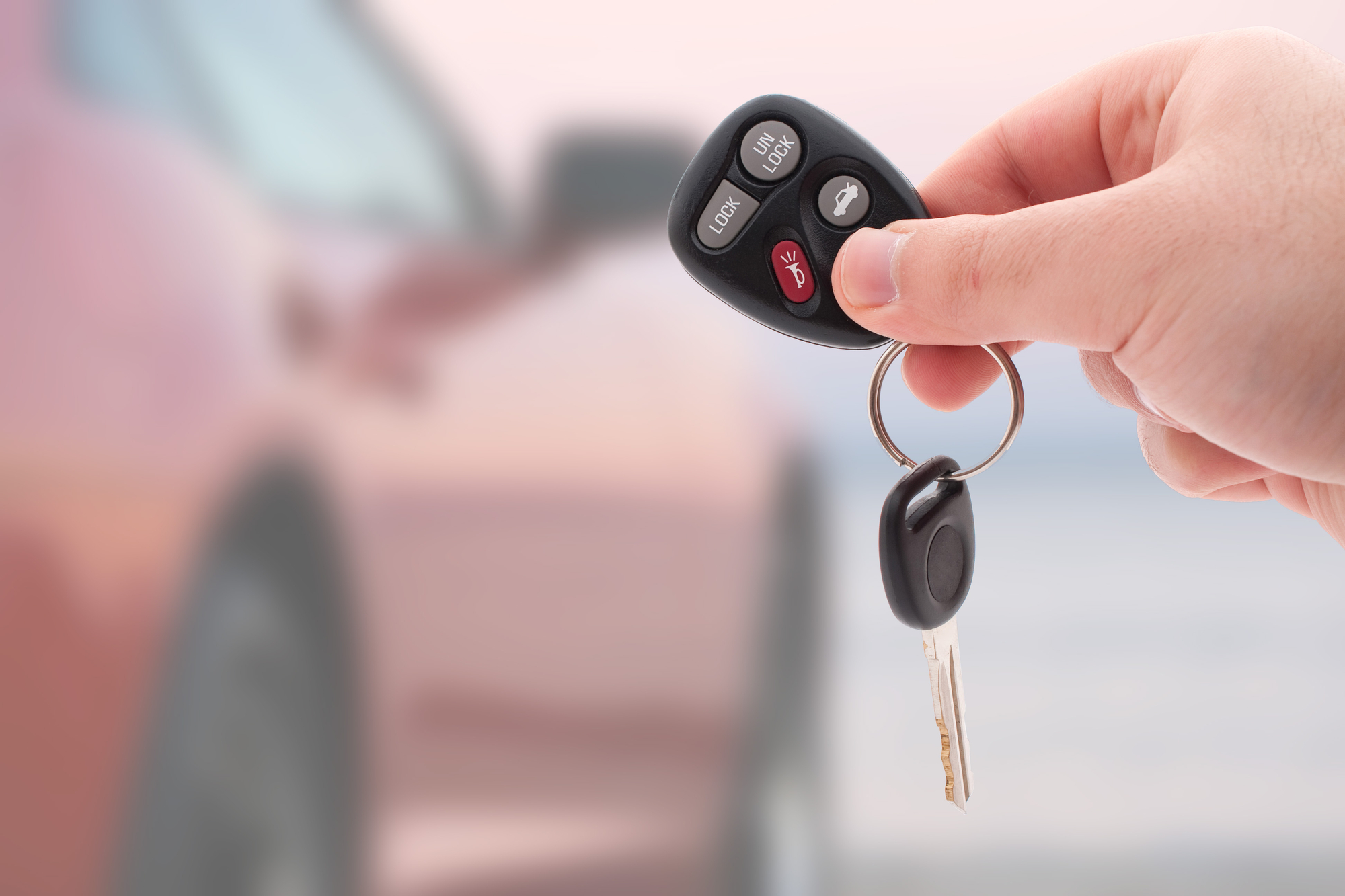 A person holding a car key in front of a leased car.